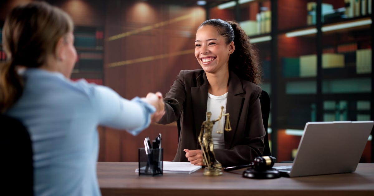 Female Lawyer And Hispanic Client Seal Judicial Agreement With Handshake